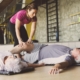 Senior couple workout in rehabilitation center. Personal trainer helps elderly couple to do stretching on the floor.