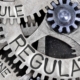 Macro photo of tooth wheel mechanism with REGULATION, LAW, RULE, AUTHORITY, GUIDELINE and STANDARD words imprinted on metal surface