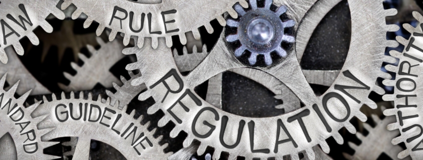 Macro photo of tooth wheel mechanism with REGULATION, LAW, RULE, AUTHORITY, GUIDELINE and STANDARD words imprinted on metal surface