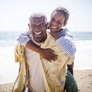 A beautiful senior black couple piggyback on the beach