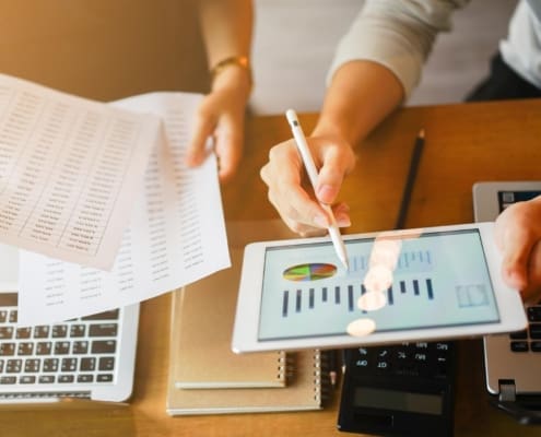 close up group of businessman use stylus pen for explaining dashboard about company's profit monthly on tablet and businesswoman holding report paper for collaborate work at meeting event , business finance concept