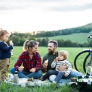 Front view of family with two small children on cycling trip, sitting on grass and resting.