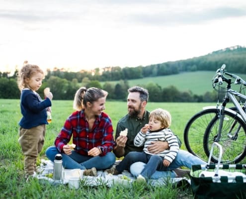Front view of family with two small children on cycling trip, sitting on grass and resting.