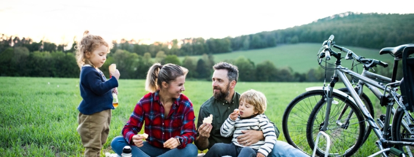 Front view of family with two small children on cycling trip, sitting on grass and resting.