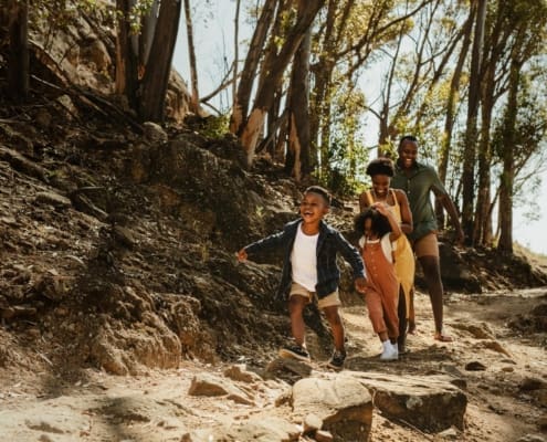 Young family running down rocky mountain trail. Two kids running with parent on a trail in forest.