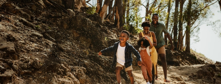 Young family running down rocky mountain trail. Two kids running with parent on a trail in forest.