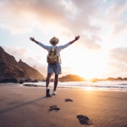 Young man arms outstretched by the sea at sunrise enjoying freedom and life, people travel wellbeing concept