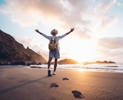 Young man arms outstretched by the sea at sunrise enjoying freedom and life, people travel wellbeing concept