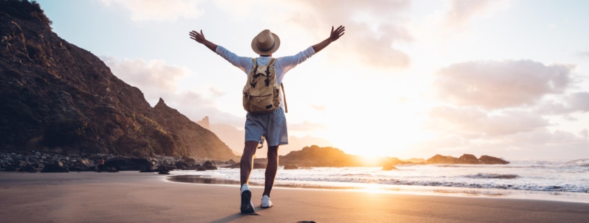 Young man arms outstretched by the sea at sunrise enjoying freedom and life, people travel wellbeing concept