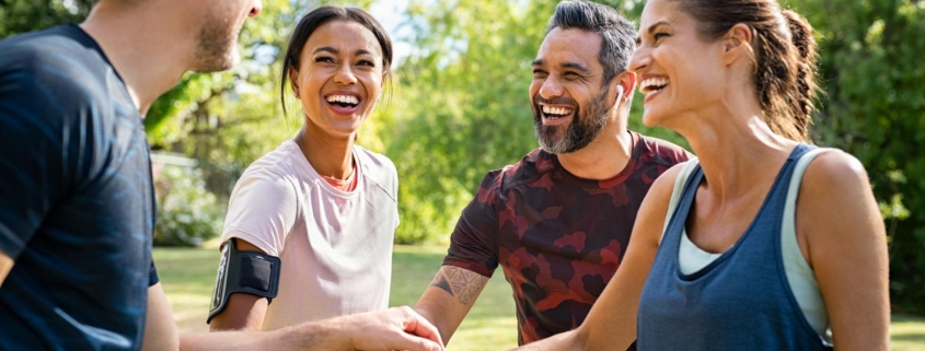 Laughing mature and multiethnic sports people putting hands together at park. Happy group of men and beautiful women smiling and stacking hands outdoor after fitness training. Multiethnic sweaty team cheering after intense training.