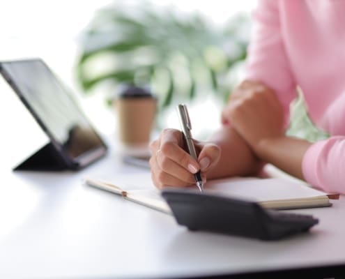 Woman in home office using tablet and mobile phone writing work schedule on notepad, Working from home.