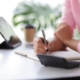 Woman in home office using tablet and mobile phone writing work schedule on notepad, Working from home.