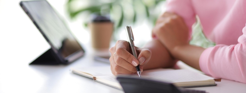 Woman in home office using tablet and mobile phone writing work schedule on notepad, Working from home.