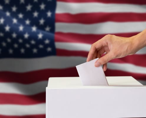 Close-up of man casting and inserting a vote and choosing and making a decision what he wants in polling box with United States flag blended in background..
