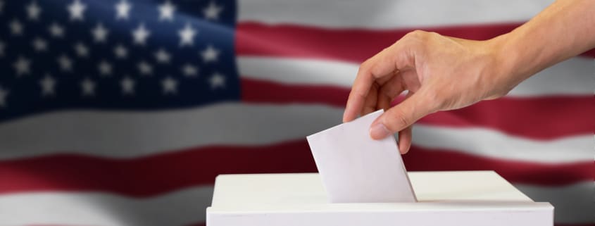 Close-up of man casting and inserting a vote and choosing and making a decision what he wants in polling box with United States flag blended in background..