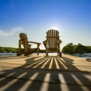 Cottage life - Sunrise on two empty Adirondack chairs sitting on a dock on a lake in Muskoka, Ontario Canada. The sun rays create long shadows on the wooden pier.