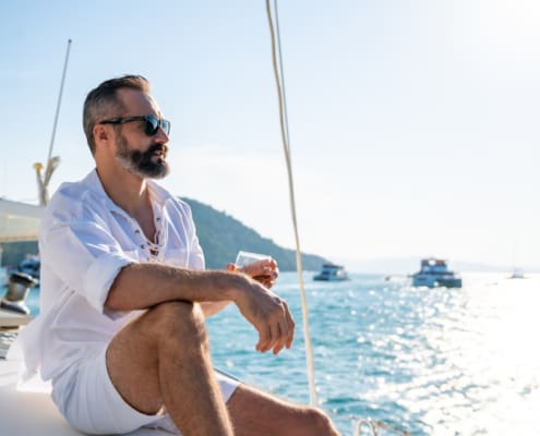 Caucasian man enjoy outdoor luxury lifestyle with alcoholic drinks while catamaran boat sailing at summer sunset. Healthy handsome male relaxing outdoor leisure activity with tropical travel vacation trip