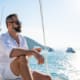 Caucasian man enjoy outdoor luxury lifestyle with alcoholic drinks while catamaran boat sailing at summer sunset. Healthy handsome male relaxing outdoor leisure activity with tropical travel vacation trip